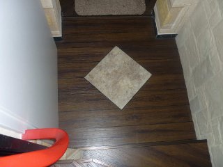 Flurbereich mit dunklem Vinylboden und einer quadratischen Dekorfliese in der Mitte. Kombination aus Holzoptik und Steinfliese für einen individuellen Look.