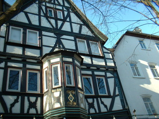 Historisches Fachwerkhaus mit restaurierter Fassade in Weiß und Dunkelgrün, dekorativen Holzbalken und aufwendig gestalteten Fensterrahmen.
