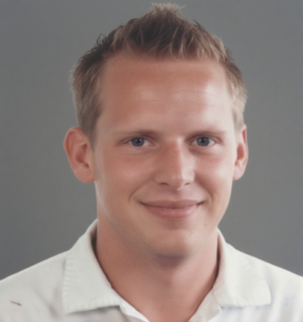 Porträt eines jungen Handwerkers im weißen Arbeitshemd vor grauem Hintergrund.